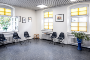 Ein Wartezimmer, in dem blaue Stühle mit etwas Abstand stehen.