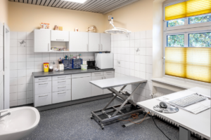 Ein Behandlungszimmer mit Schränken und Geräten im Hintergrund.