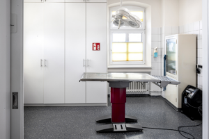Ein Behandlungszimmer mit einem Behandlungstisch in der Mitte, über dem eine Lampe hängt