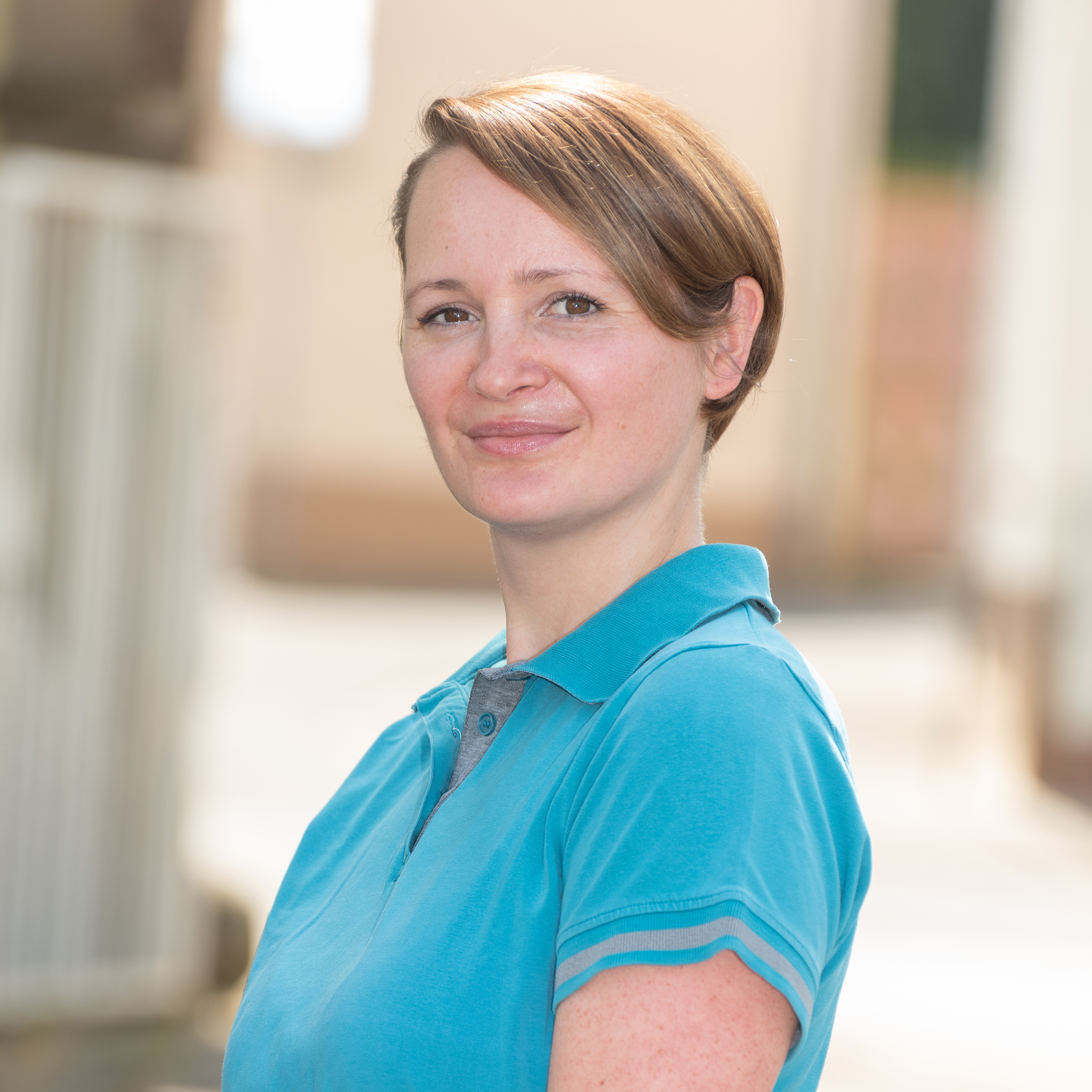 Porträtfoto von TFA Sandra Sonderschäfer der Tierarztpraxis Zieris, lächelnd in blauem Praxis-Kasack vor hellem Hintergrund