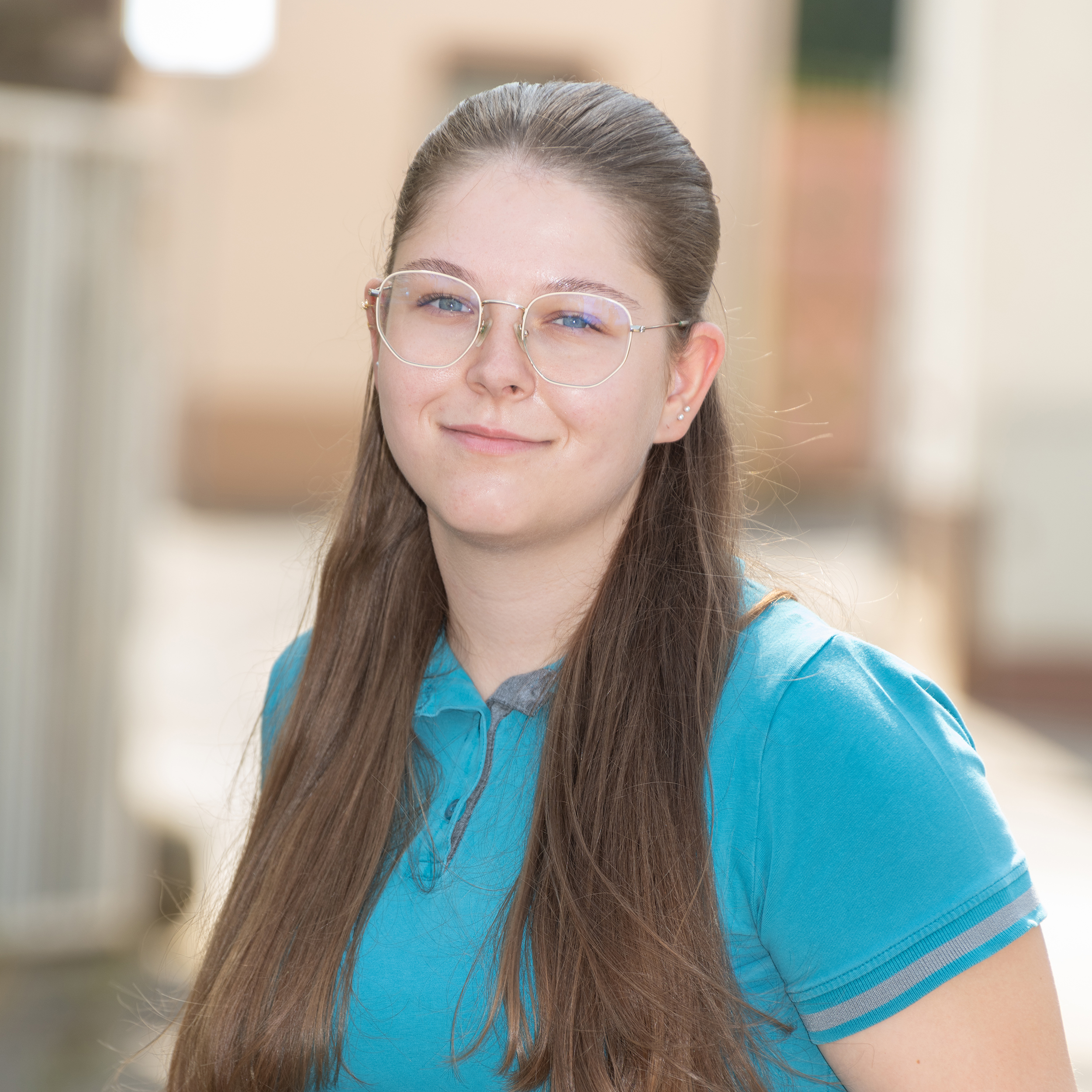 Porträtfoto von TFA Vanessa Heuschele der Tierarztpraxis Zieris, lächelnd in blauem Praxis-Kasack vor hellem Hintergrund