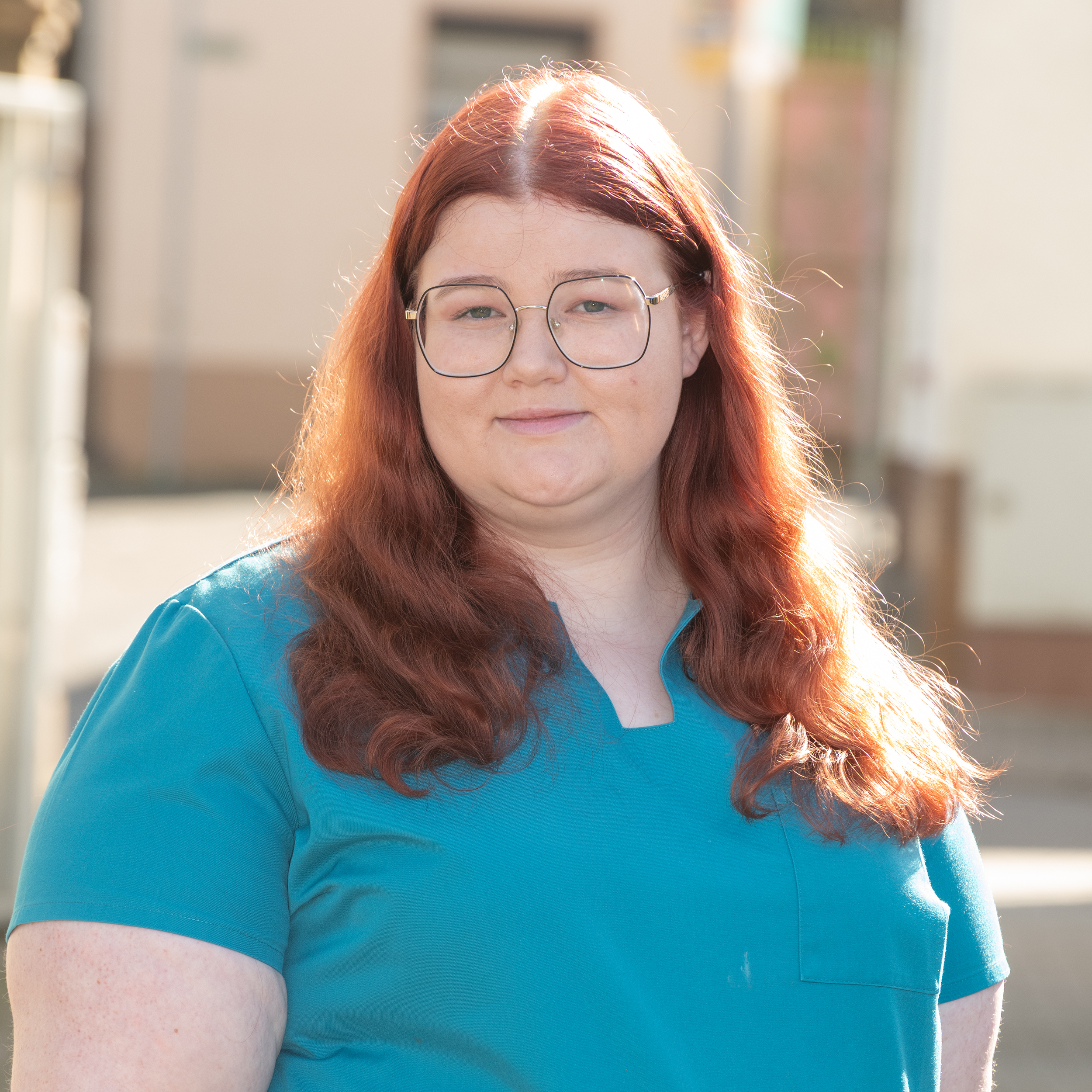 Porträtfoto von TFA Xenia Minke der Tierarztpraxis Zieris, lächelnd in blauem Praxis-Kasack vor hellem Hintergrund